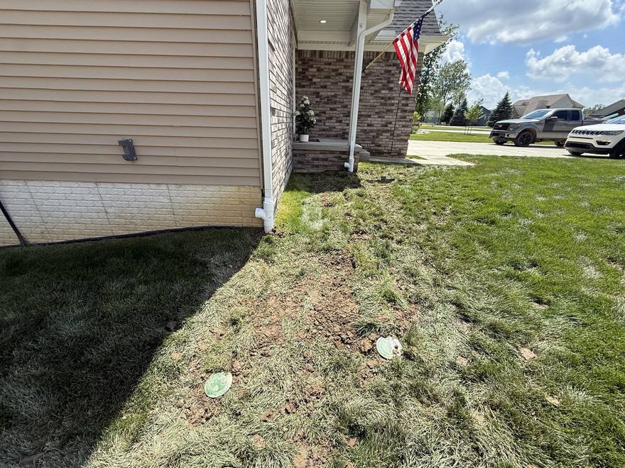 The same corner after the install: both downspouts drop into buried lines at the foundation, with the trench lines crossing the lawn to two green pop-up emitters.