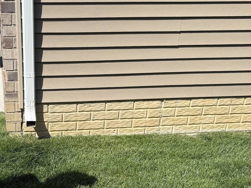 Downspout on the driveway side of a Canton, Michigan home ending in a short elbow that empties right against the foundation.